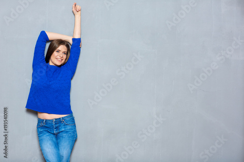 Smiling girl posing against gray wall background with hands risi