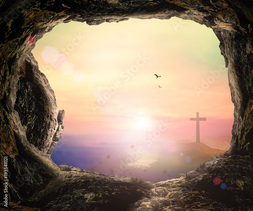 Resurrection of Easter Sunday concept: The cross and empty tomb stone over mountain sunrise background 