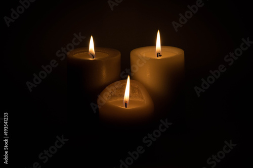 Set of three burning candles against a dark background