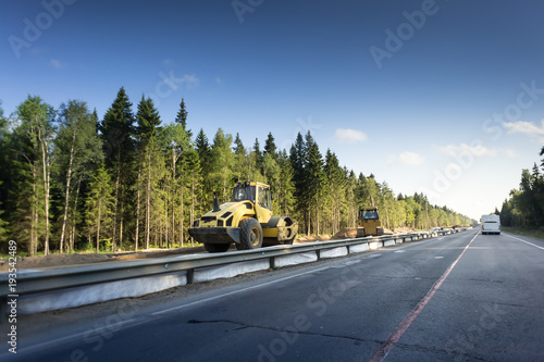 Bulldozer machine during construction road works. metal safety barrier and green forest photo