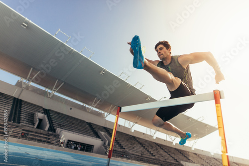 Athlete jumping over an hurdle on running track photo