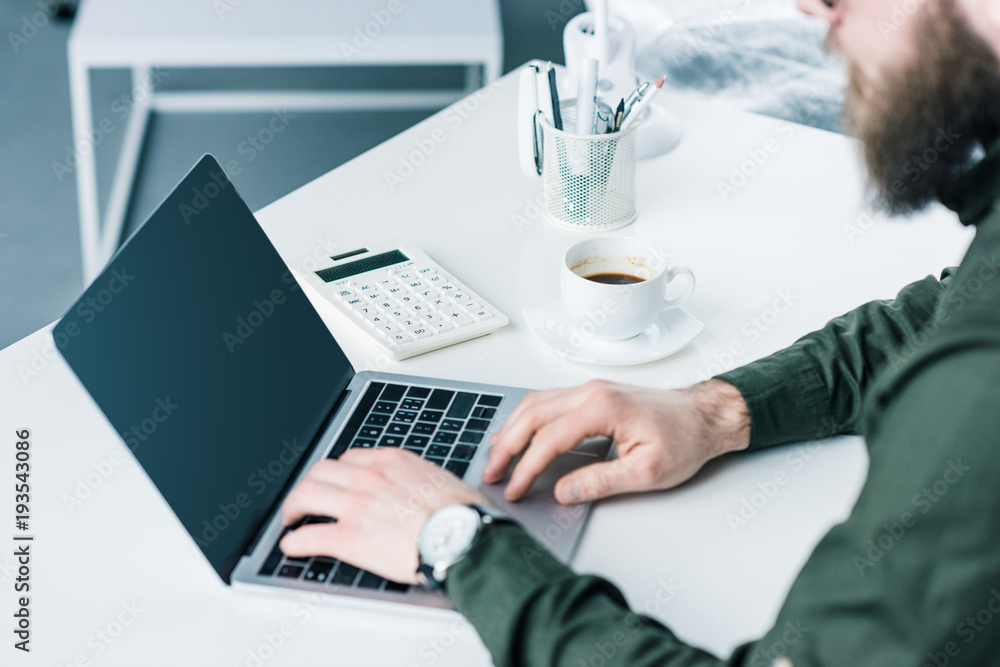 partial view of businessman working on laptop with blank screen at workplace partial view of businessman working on laptop with blank screen at workplace