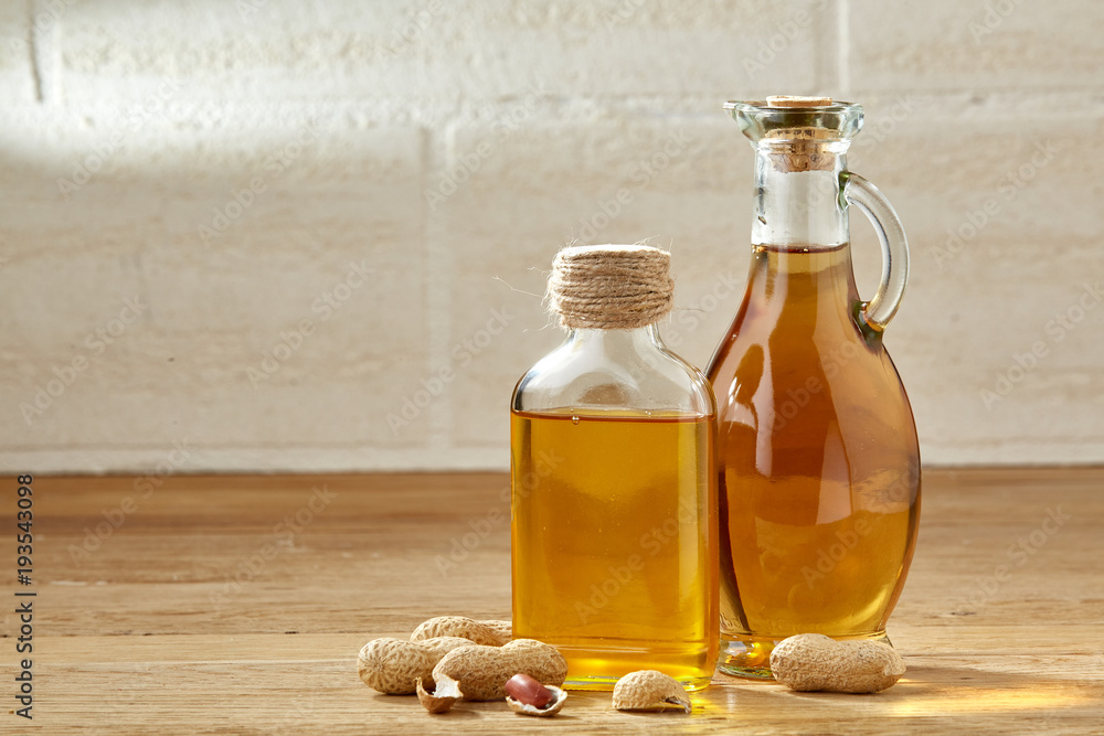 Aromatic oil in a glass jar and bottle with peanuts on wooden table, close-up. Aromatic oil in a glass jar and bottle with peanuts on wooden table, close-up.