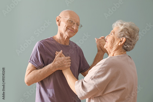 Cute elderly couple dancing against color background