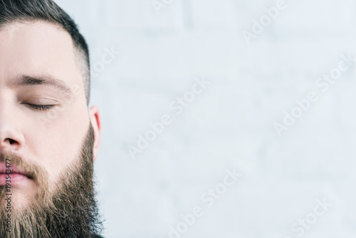 cropped shot of bearded man with eyes closed against white brick wall