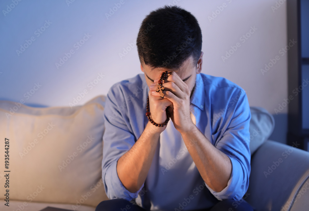 Religious young man with rosary beads praying at home Religious young man with rosary beads praying at home
