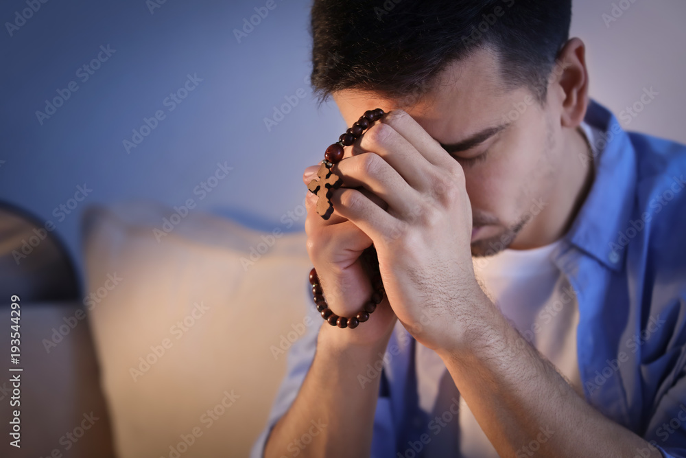 Religious young man with rosary beads praying at home
