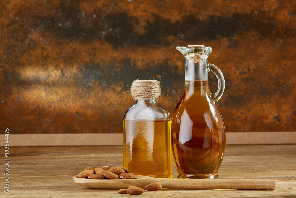 Aromatic oil in a glass jar and bottle with almond in a scoop on wooden table, close-up. Aromatic oil in a glass jar and bottle with almond in a scoop on wooden table, close-up.