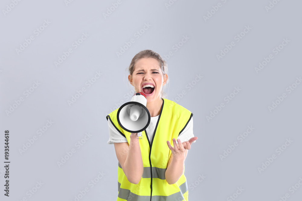 Fototapeta premium Young woman in reflective vest shouting into megaphone on grey background