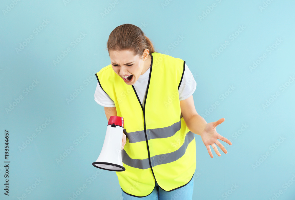 Young woman in reflective vest shouting into megaphone on color background Young woman in reflective vest shouting into megaphone on color background