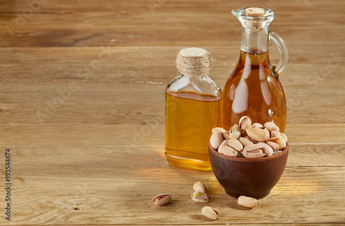 Aromatic oil in a glass jar and bottle with pistachios in bowl on wooden table, close-up. photo