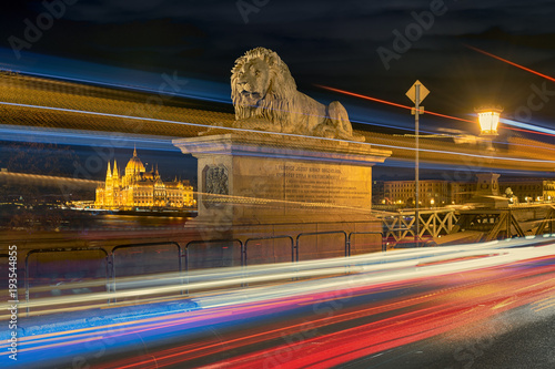 Lion statue on Budapest Chain bridge against Parliament building through bright traffic motion lights photo