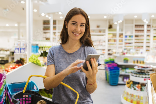 Casual young female, using her cellphone in modern supermarket. Looking at camera