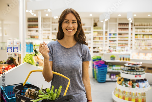Pretty young woman in the modern food supermarket, with her basket. Face camera