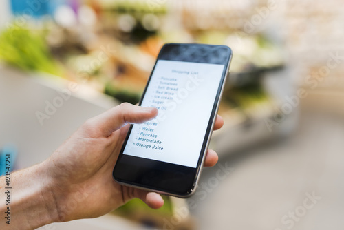 Woman using her mobile phone in supermarket while shopping. Shopping list. Close-up hand