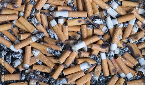 Gerauchte Zi­ga­ret­ten­stum­mel liegen in Asche - Hintergrund photo