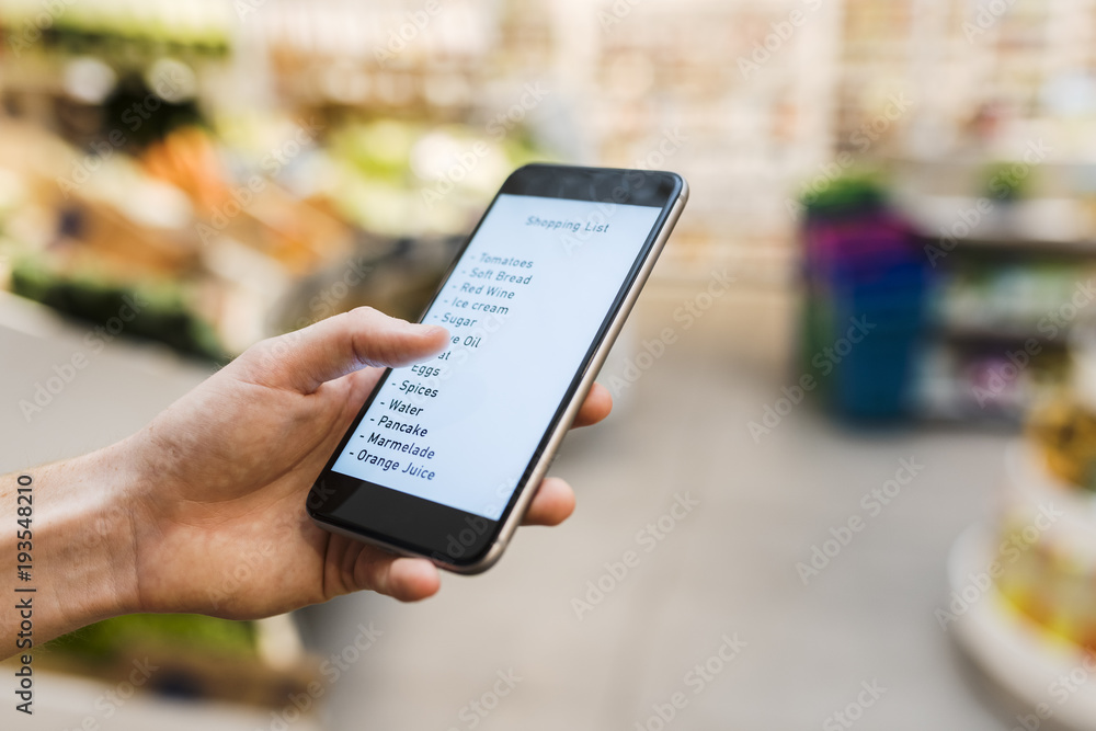 Female using smart phone while shopping in supermarket. Shopping list. Close-up hand