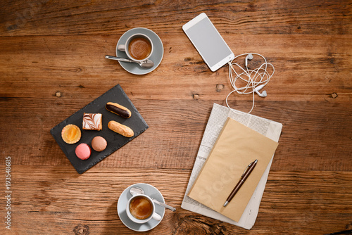 above view still life of two espresso coffee with macaroons and french pastries on a rustic wooden tables with smartphone earphone book and newspaper