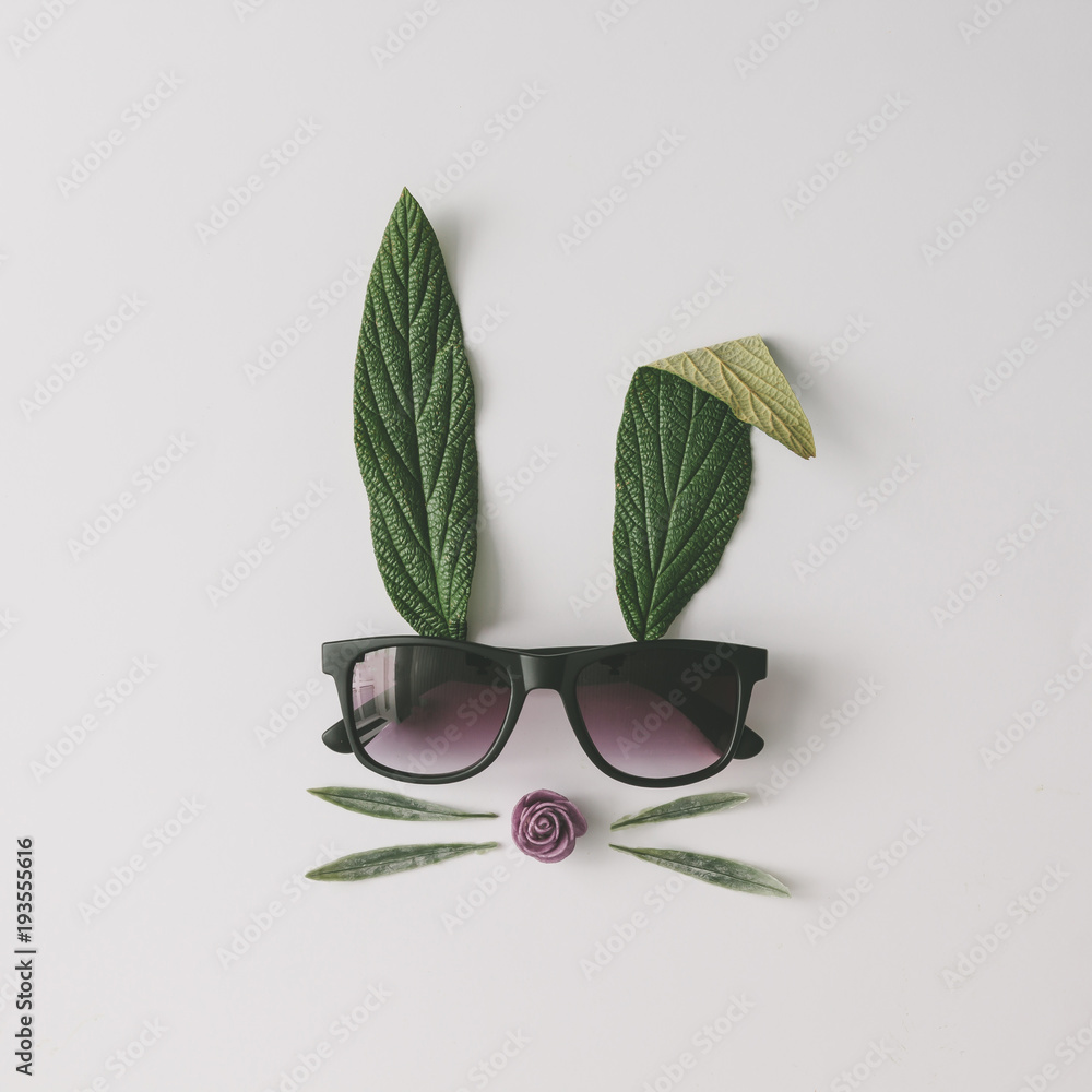 Fototapeta premium Bunny rabbit face made of natural green leaves with sunglasses on bright background. Easter minimal concept. Flat lay.