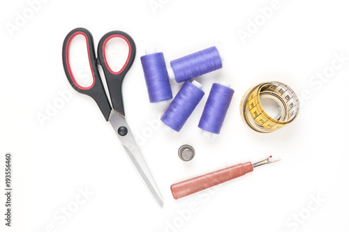 Sewing supplies and tools, medium purple sewing threads, yellow measuring tape with black numbers, big scissors, metal thimble and seam ripper on a white background