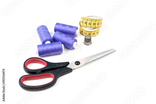 Sewing supplies and tools, medium purple sewing threads, yellow measuring tape with black numbers, big scissors and metal thimble on a white background