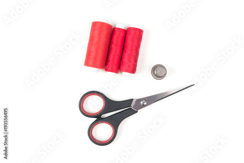 Read sewing threads with black scissors and metal thimble on a white background