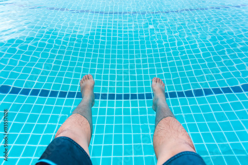 A man put his legs in pool for relax.