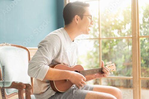 Asian young man hands playing acoustic guitar ukulele at home. Enjoy playing acoustic guitar sunshine in the evening.. photo
