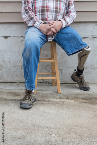 Leg amputee sitting on stool with prosthetic leg to the side, copy space, vertical aspect