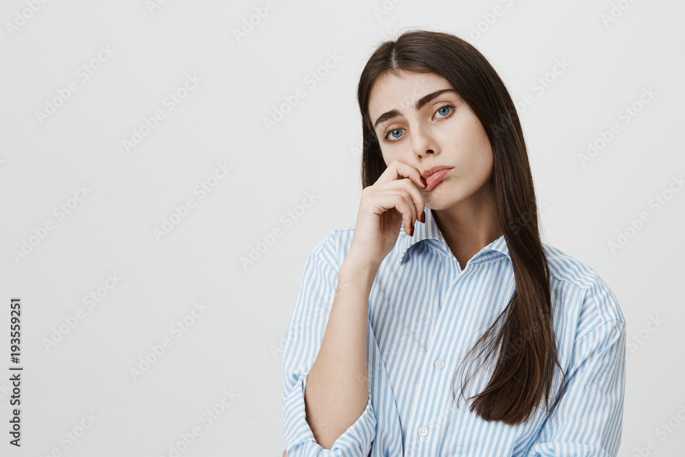 Indoor portrait of sexy adult woman with bored and tired expression, holding hand near lips and standing over gray background in blue striped shirt. Girl annoyed after hearing out useless information Indoor portrait of sexy adult woman with bored and tired expression, holding hand near lips and standing over gray background in blue striped shirt. Girl annoyed after hearing out useless information