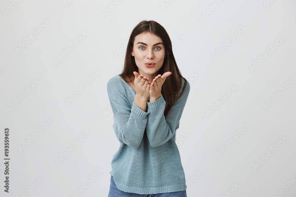 Attractive european young woman throws a kiss bending towards camera and gesturing with hands, standing over gray background. Excited and happy mom sends kiss to her cute daughter Attractive european young woman throws a kiss bending towards camera and gesturing with hands, standing over gray background. Excited and happy mom sends kiss to her cute daughter