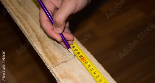 Man marking point on plank with pencil and measure tape