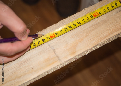 Closeup of using roulette to measure wood board and make a mark with pencil