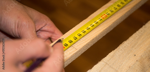 Hands holding ruler on wooden plank and making a mark with a pencil