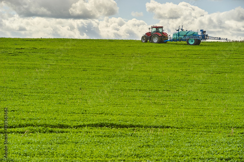 Tractor spraying pesticides on field with sprayer at spring