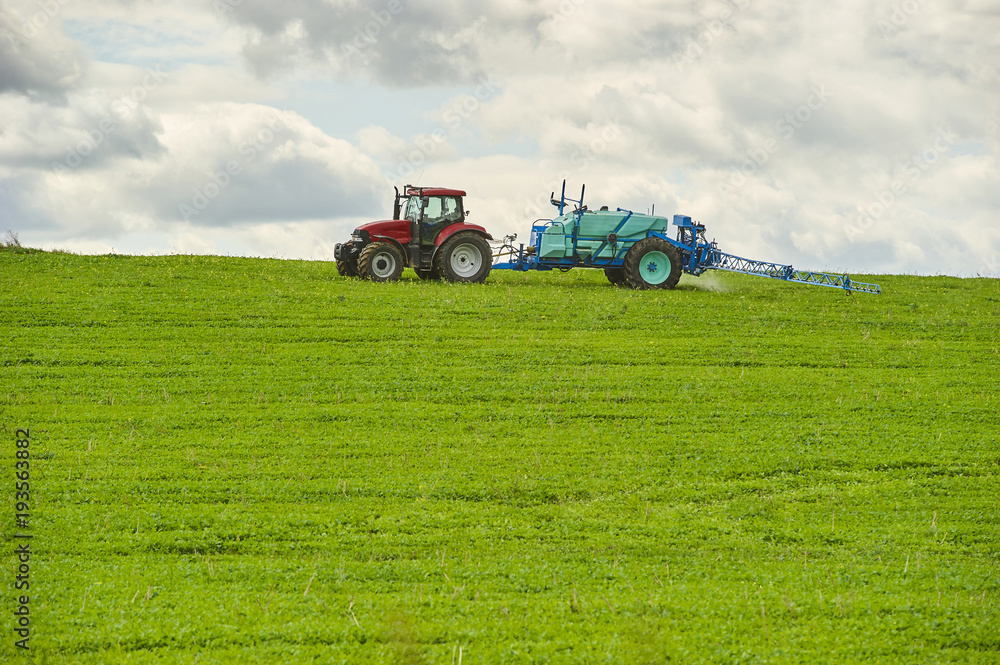 Fototapeta premium Tractor spraying pesticides on field with sprayer at spring