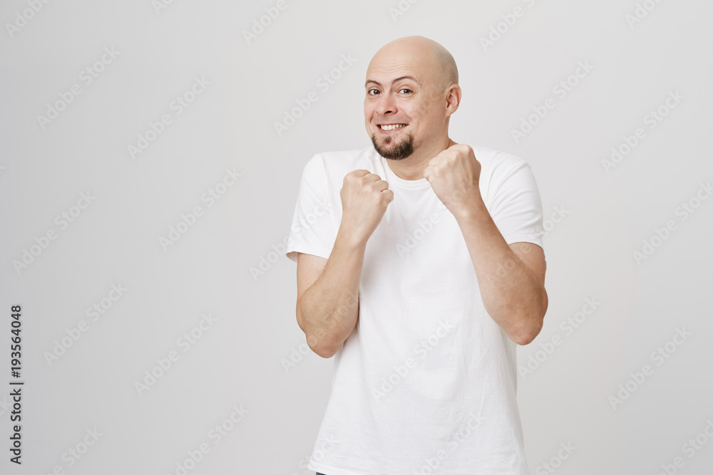 Indoor portrait of charming playful bald caucasian bearded man standing in boxer pose defending, faking fight and standing over gray background. Joyful guy waiting for attack Indoor portrait of charming playful bald caucasian bearded man standing in boxer pose defending, faking fight and standing over gray background. Joyful guy waiting for attack