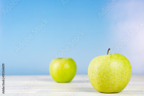 Two green apples on wooden table, blue sky background