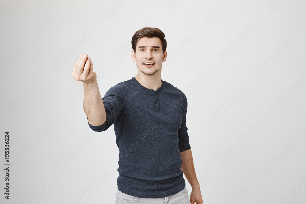 Indoor shot of serious looking guy giving speech, showing italian gesture with raised hand, standing over gray background. Actor performing play in front of audience in theatre Indoor shot of serious looking guy giving speech, showing italian gesture with raised hand, standing over gray background. Actor performing play in front of audience in theatre