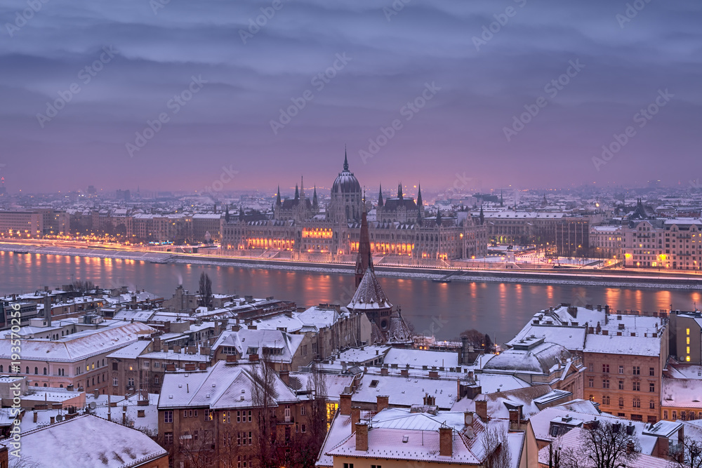Fototapeta premium Break of the day in Budapest city in winter, roofs covered with snow, river, Parliament