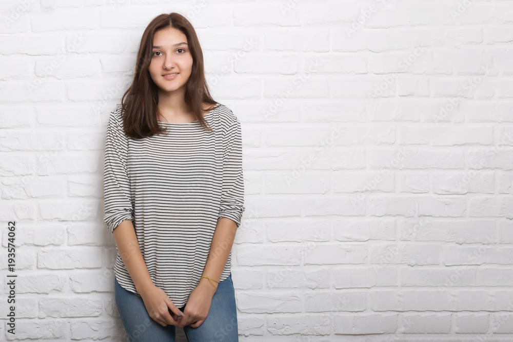A young pretty smiling girl against a white loft-style brick wall. She looks at the viewer. Copy space. A young pretty smiling girl against a white loft-style brick wall. She looks at the viewer. Copy space.