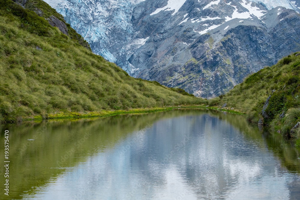 The reflection of the rocky mountain with snow on the small lake on the high mountain in Mt Cook National Park (Muller hut track)