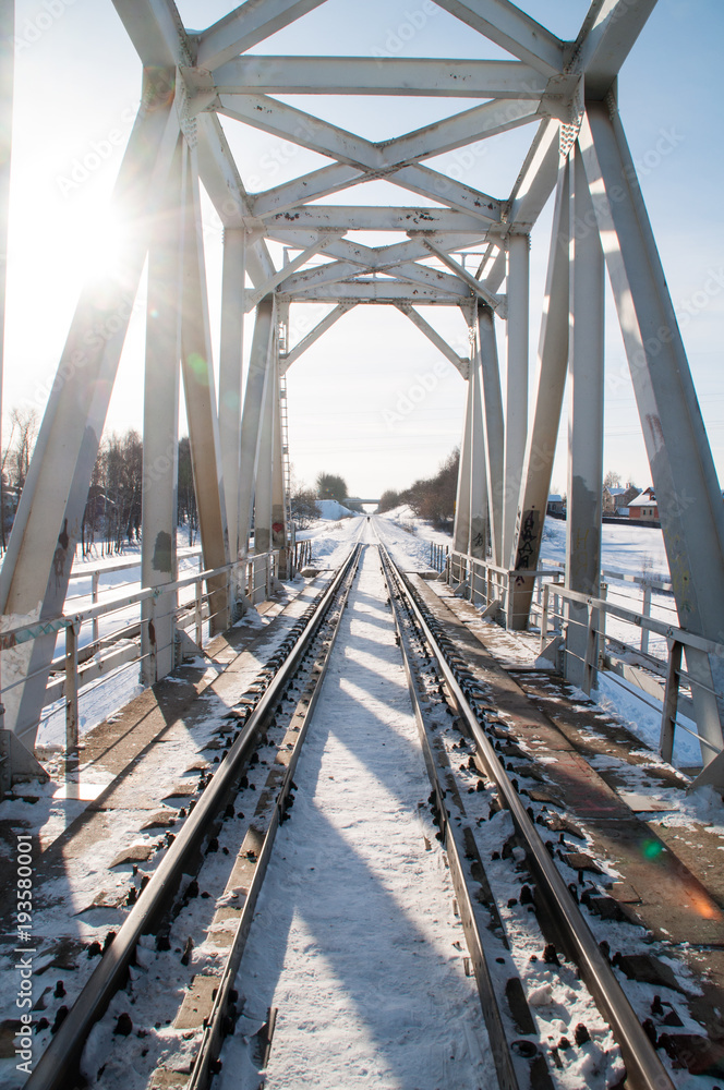 Obraz premium Winter landscape with railroad bridge over frozen river, snow-covered trees
