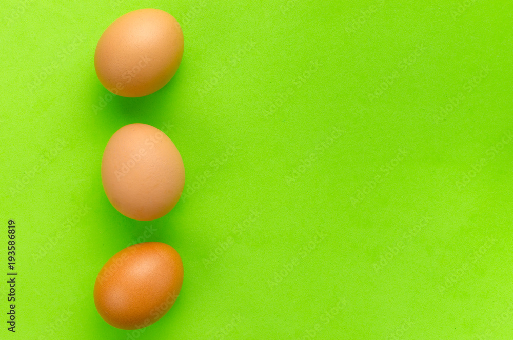 Three brown eggs on bright light green background