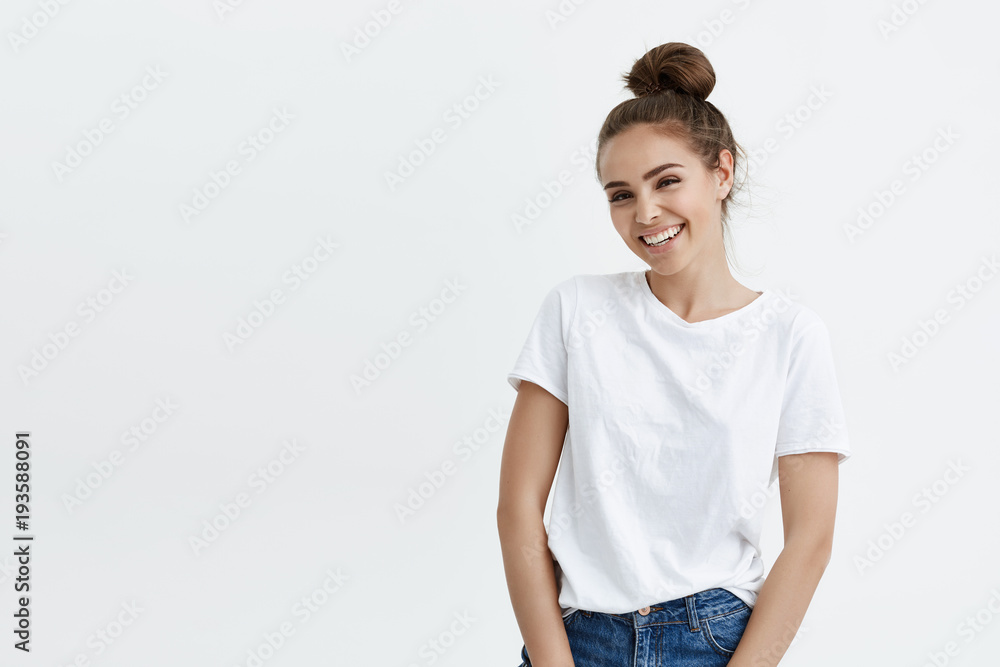 Portrait of elegant modern european woman with bun hairstyle smiling broadly at camera, expressing excitement while standing against white background. Young mom looks at her cute son playing with dog Portrait of elegant modern european woman with bun hairstyle smiling broadly at camera, expressing excitement while standing against white background. Young mom looks at her cute son playing with dog
