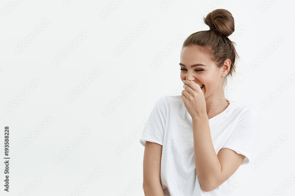 Studio portrait of playful feminine caucasian woman laughing while looking at copy space and covering mouth with hand, standing over white background. Elegant visagist talks with customer Studio portrait of playful feminine caucasian woman laughing while looking at copy space and covering mouth with hand, standing over white background. Elegant visagist talks with customer