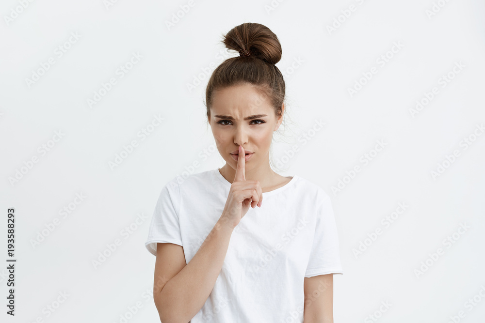 Worried cute european woman holding index finger over lips, asking stay quiet while frowning, being anxious and serious, standing over white background. Girl has terrible headache so she needs silence Worried cute european woman holding index finger over lips, asking stay quiet while frowning, being anxious and serious, standing over white background. Girl has terrible headache so she needs silence