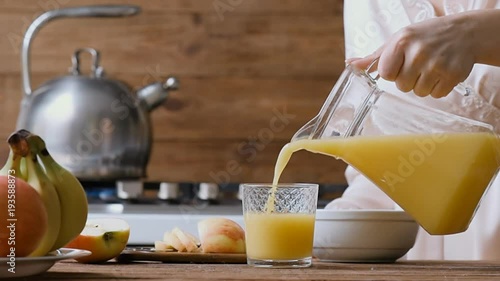 Young woman pouring the orange juice into a glass. Breakfast. 