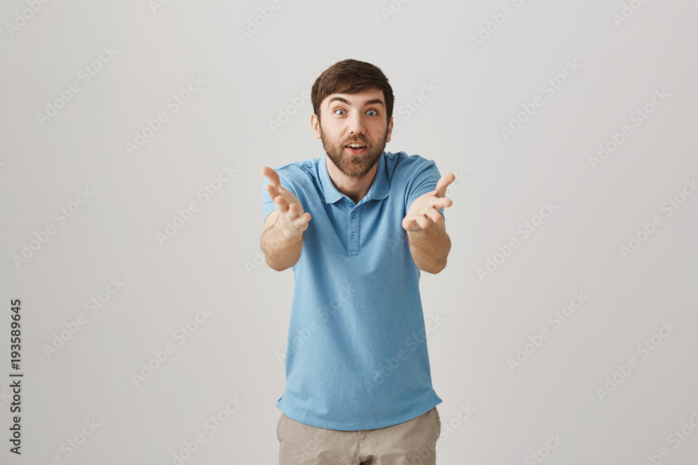 Fototapeta premium Impressed excited european worker gesturing towards camera as if talking about person, being amazed and happy while standing over gray background. Guy congratulate friend that did something great