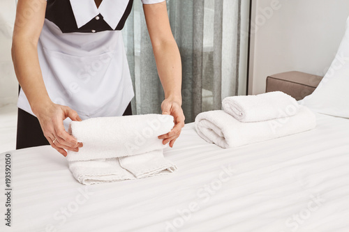 Cropped portrait of housecleaner rolling towels on bed while cleaning bedroom and preparing everything for clients to move in, making room look neat and tidy. Maid on duty trying her best